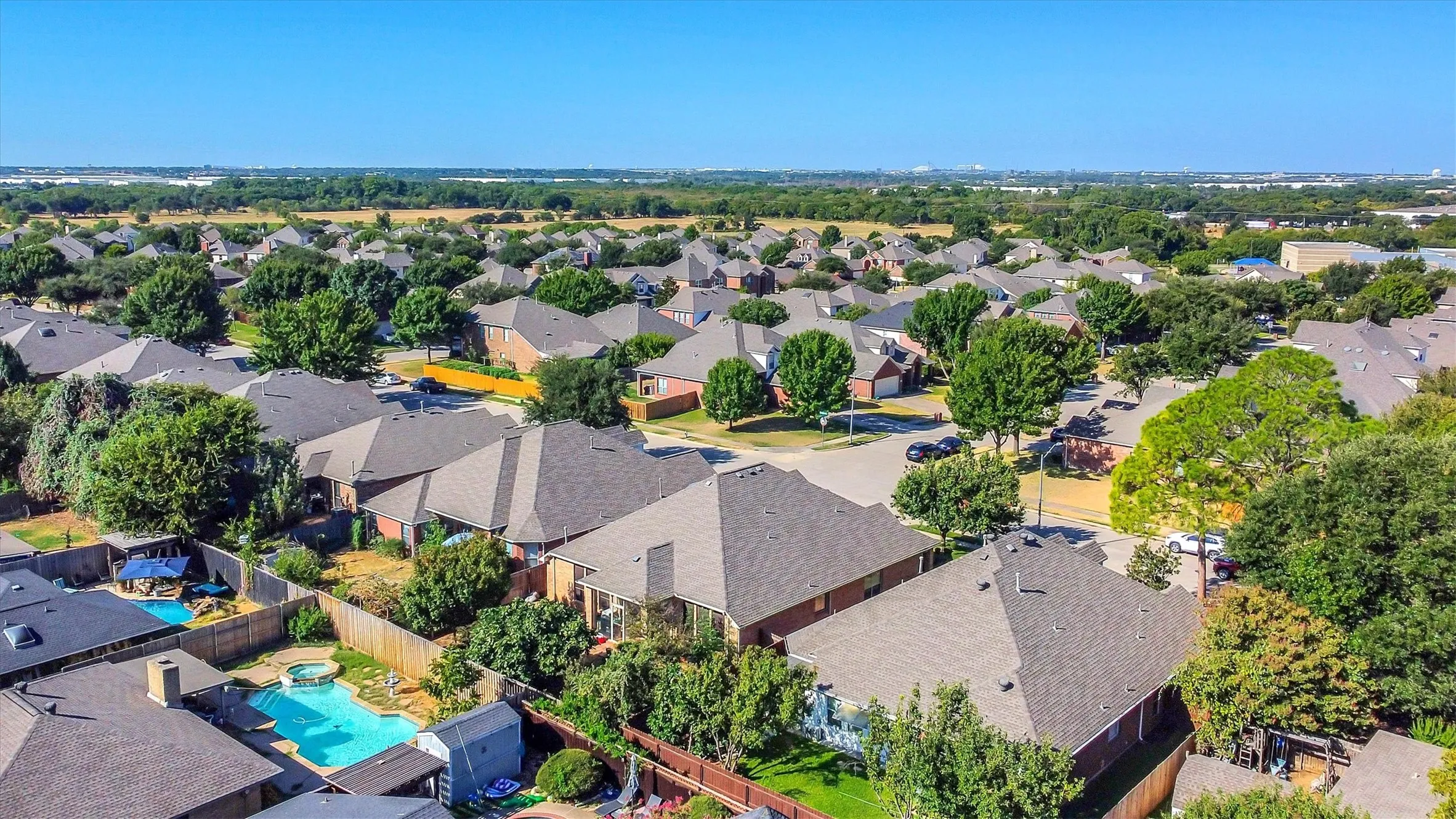 Residential neighborhood setting with mature trees and visible backyard pools