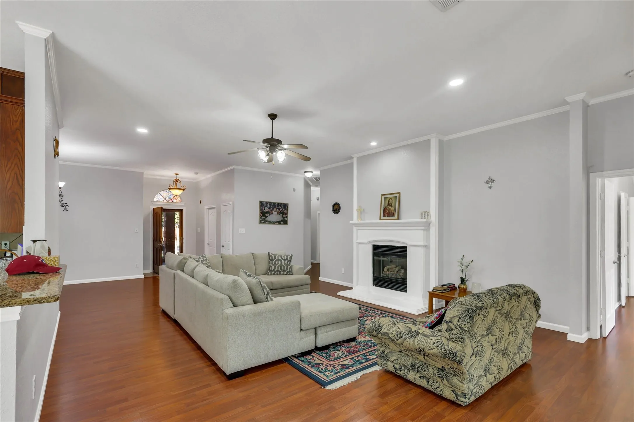 Spacious living area featuring wood-finish flooring, a built-in fireplace with a white mantel, recessed lighting, and crown molding