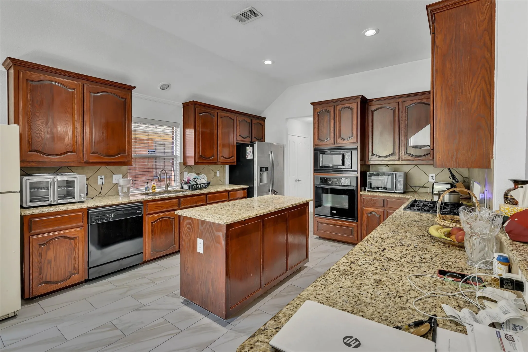 Spacious kitchen featuring rich wood cabinetry, granite countertops, a central island, stainless steel appliances, and tile flooring