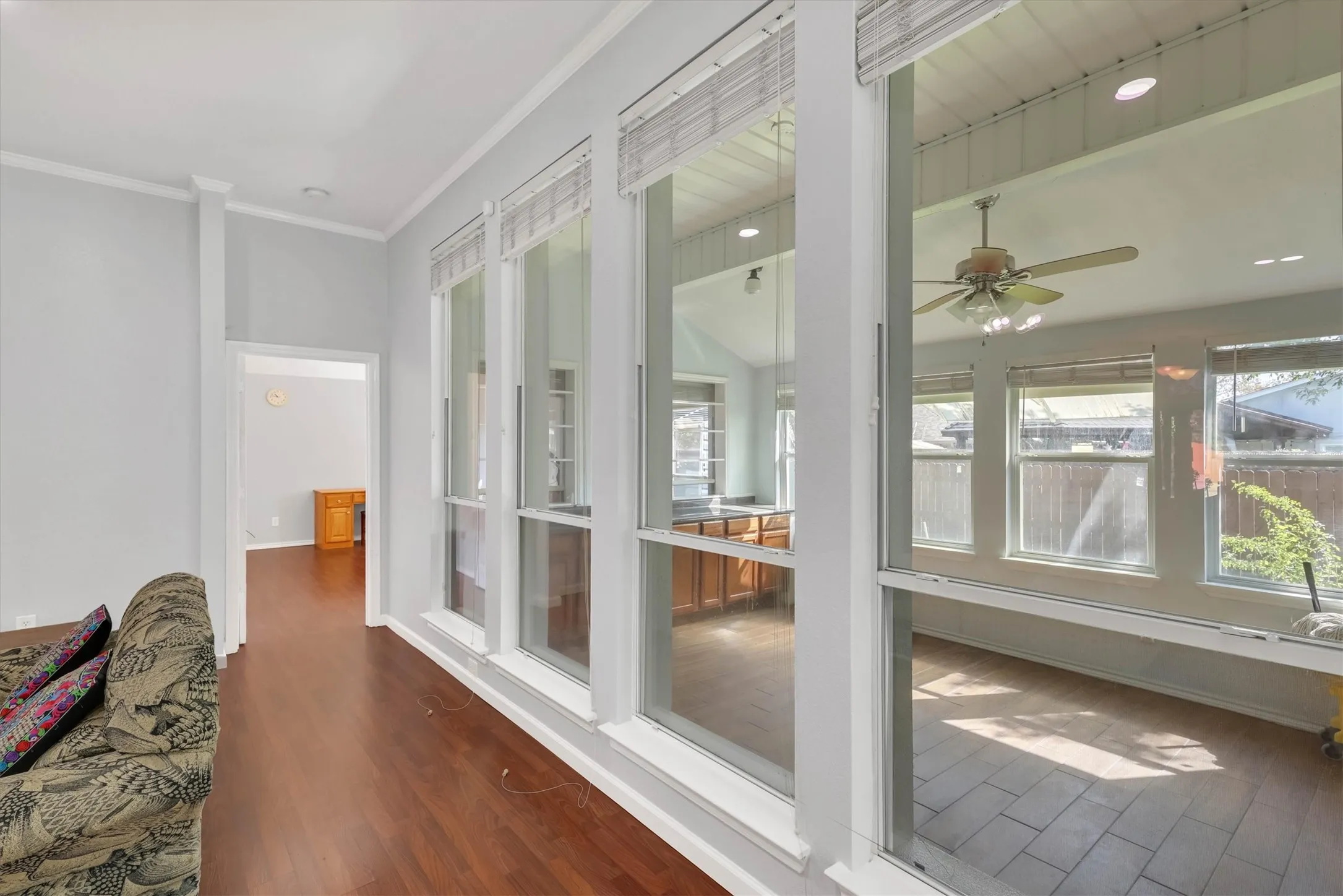 Wood-finish flooring throughout, featuring a series of tall windows, a sunroom with vaulted ceiling, ceiling fan, and tiled flooring
