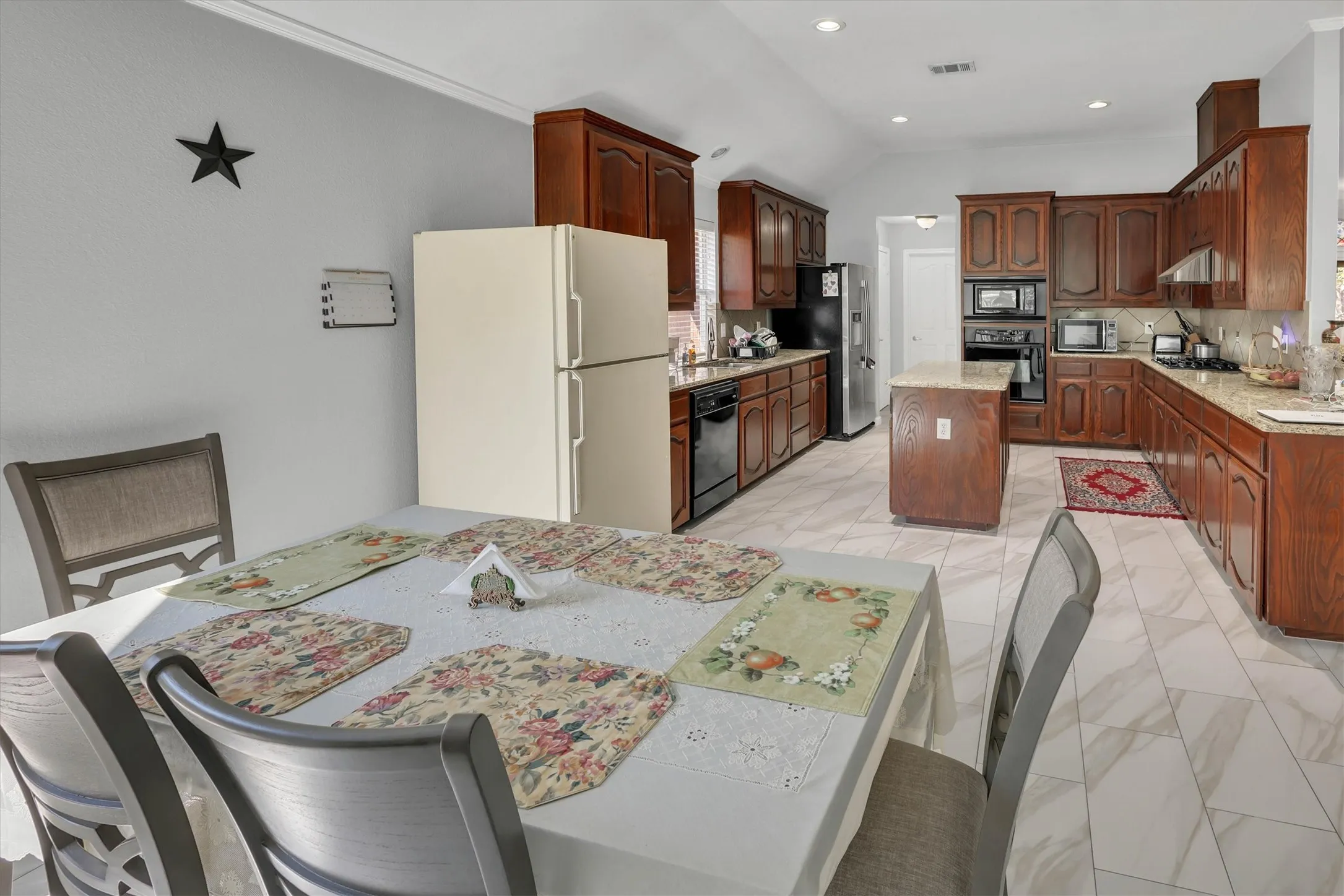 Spacious kitchen featuring wood cabinetry, light-toned countertops, a central island, built-in appliances, and light-colored tile flooring