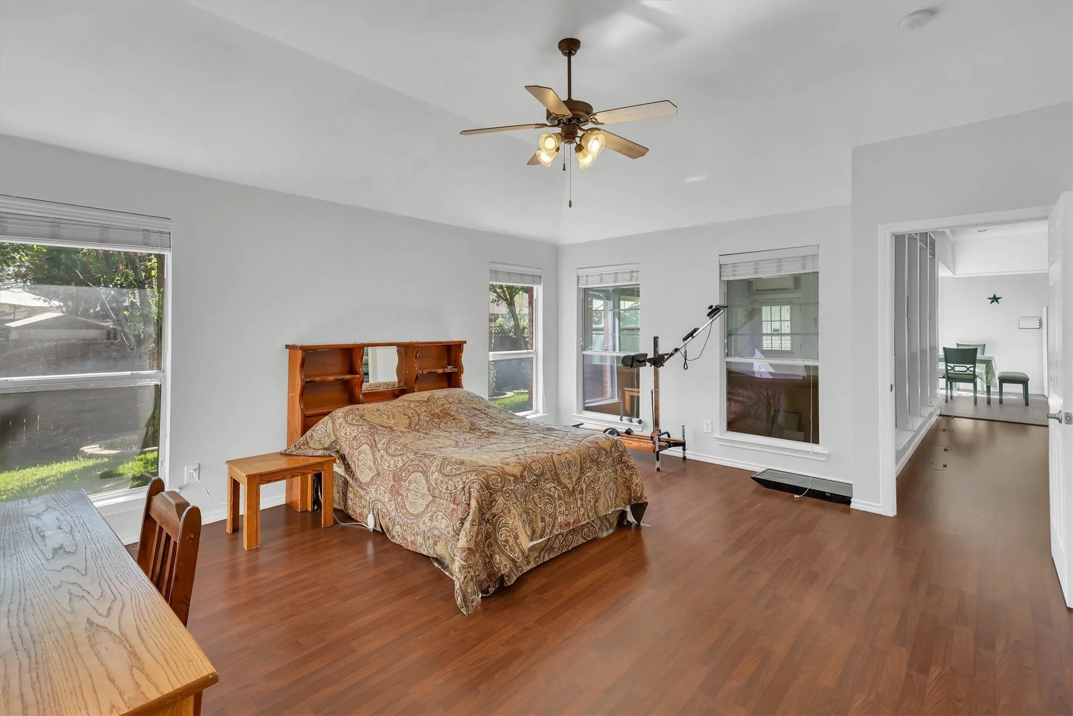 Vaulted ceiling featuring a ceiling fan with integrated lighting, wood-finish flooring, and multiple large windows with horizontal blinds