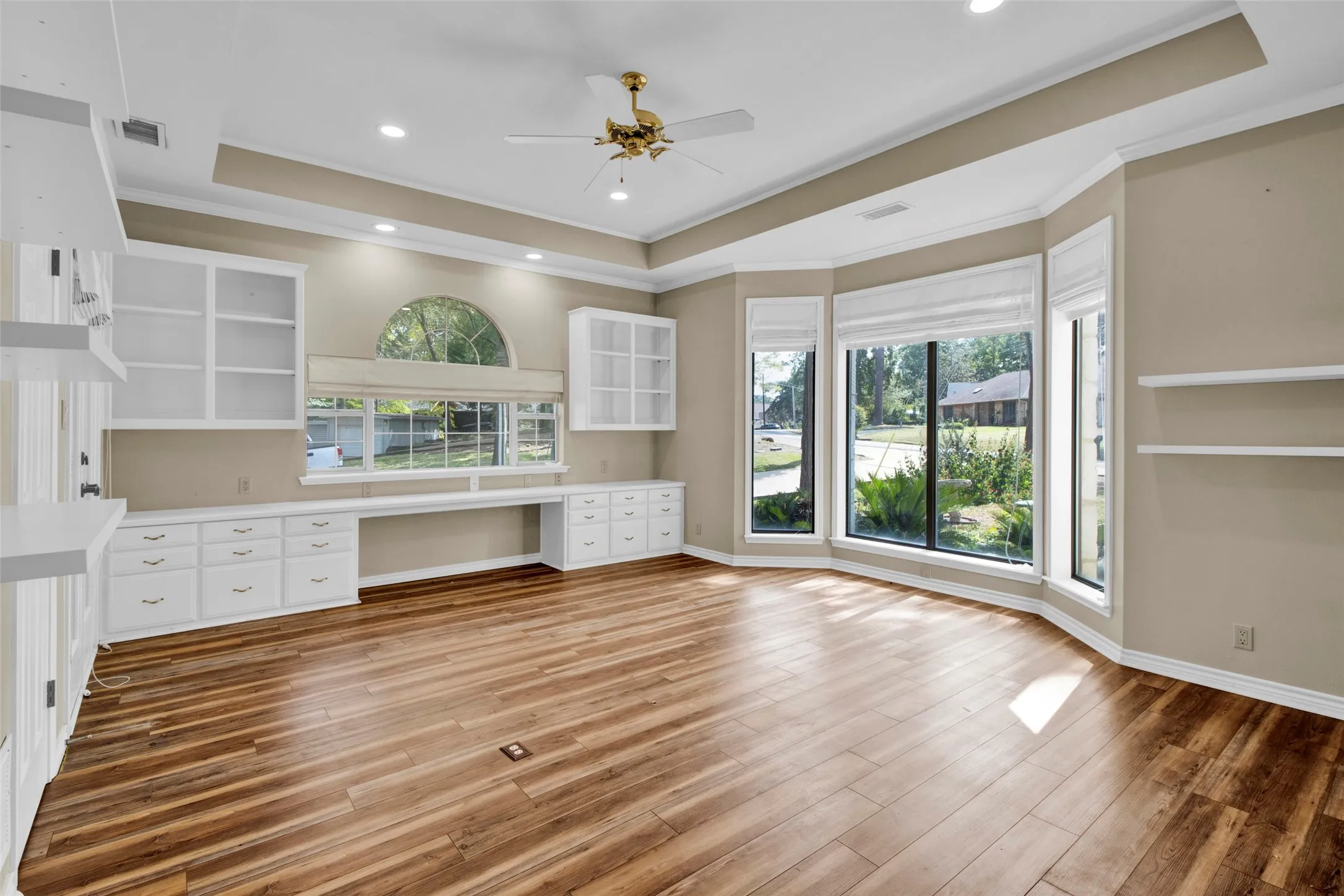 Wood-finish flooring, extensive built-in cabinetry with shelving, recessed lighting, ceiling fan, and bay windows