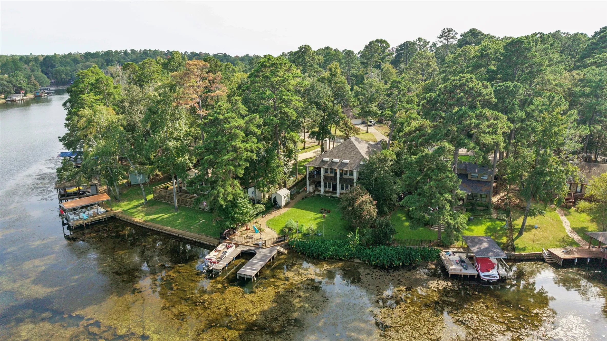 Waterfront property featuring a prominent main residence with a columned front facade, mature trees, a manicured lawn, and multiple private boat docks