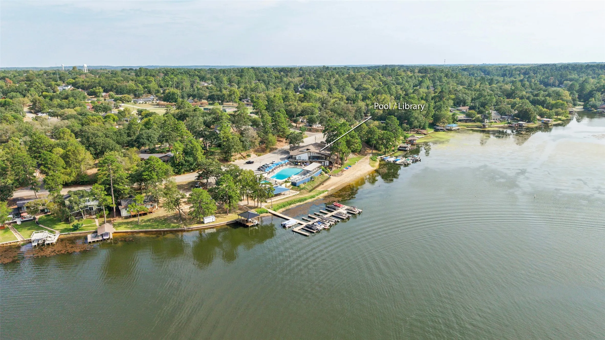 Waterfront Clubhouse & Library featuring extensive tree coverage, a private dock, and an adjacent community pool