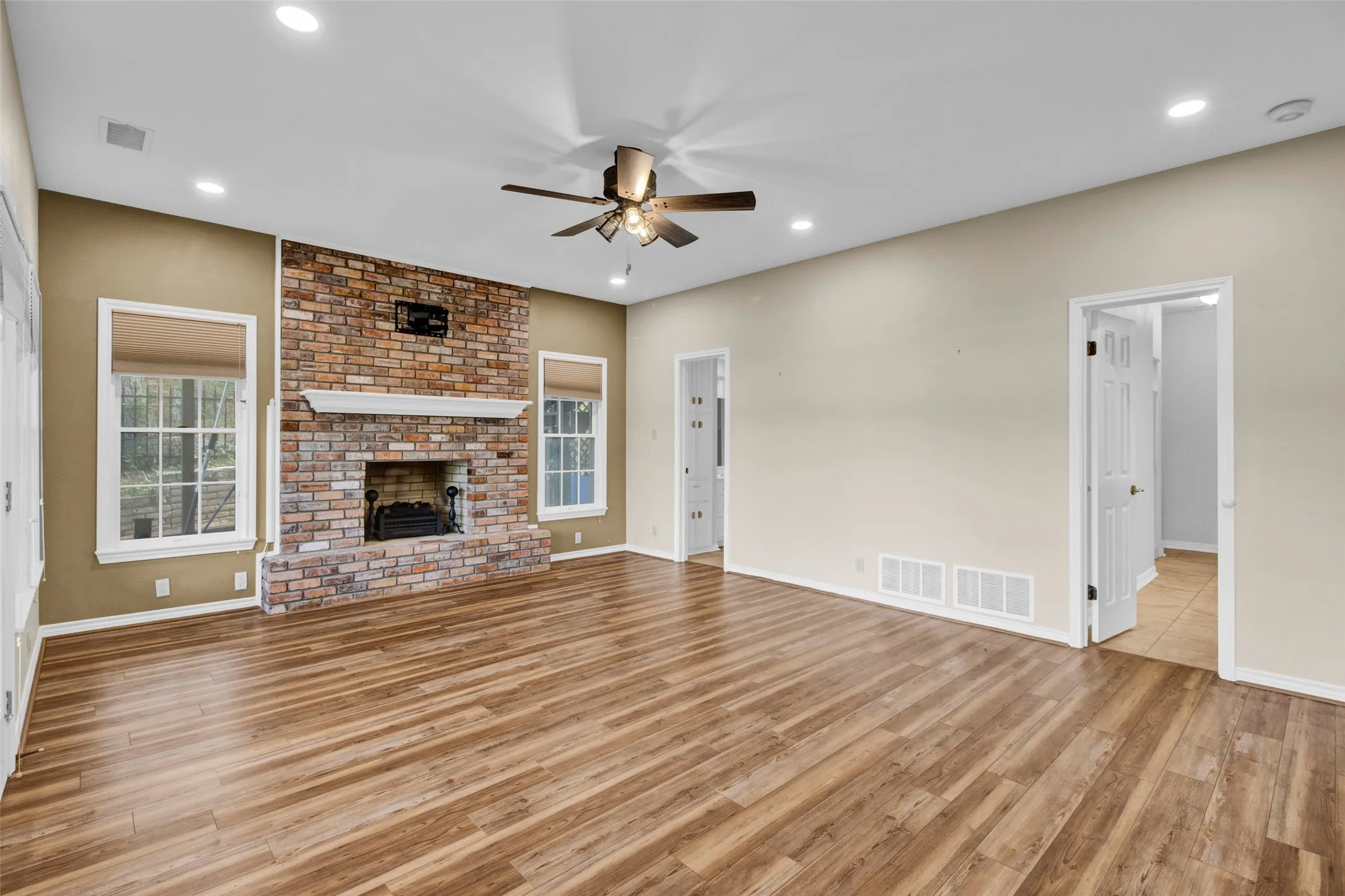Spacious living area featuring wood-finish flooring, a brick fireplace with a white mantel, and recessed lighting