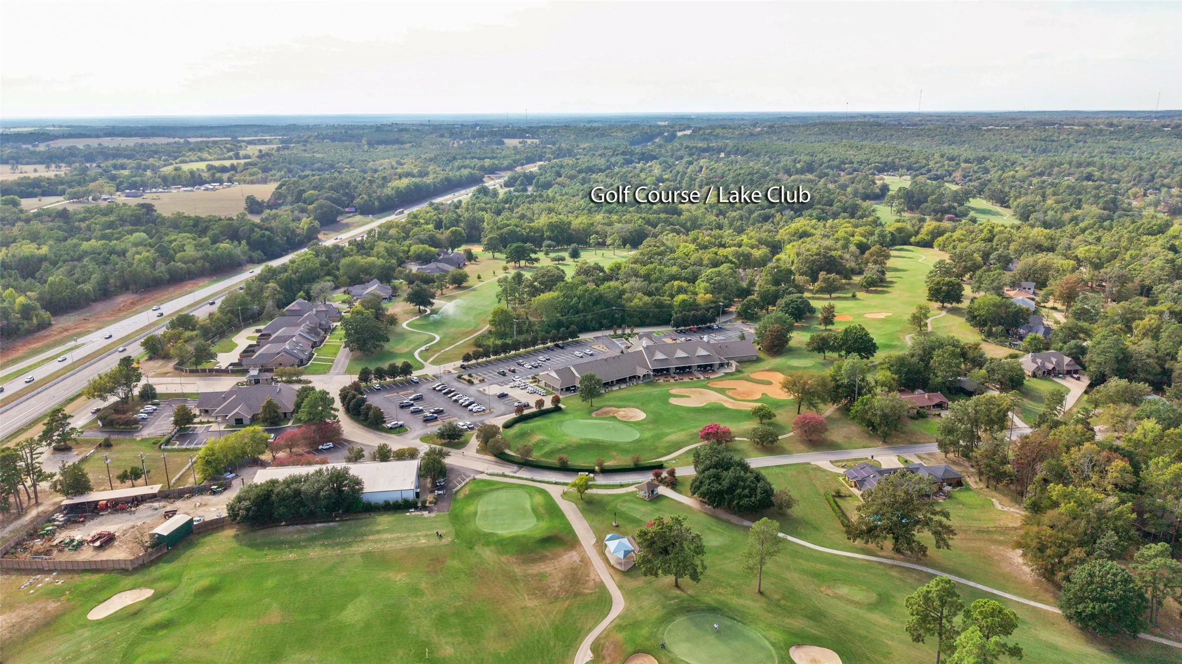 Expansive aerial perspective featuring a golf course, surrounding wooded areas, and a multi-lane highway