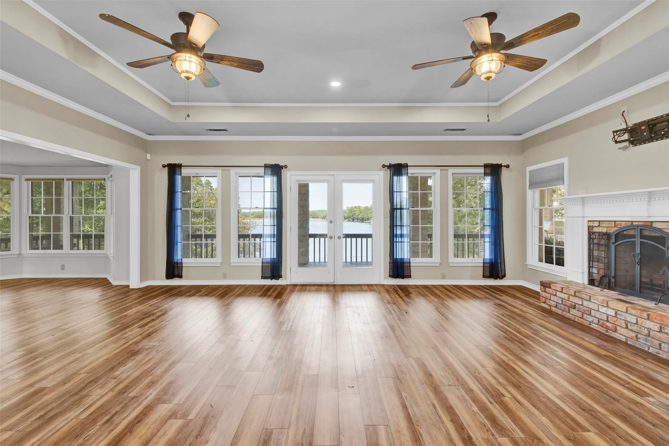 Expansive wood-finish flooring, dual ceiling fans, and a brick fireplace
