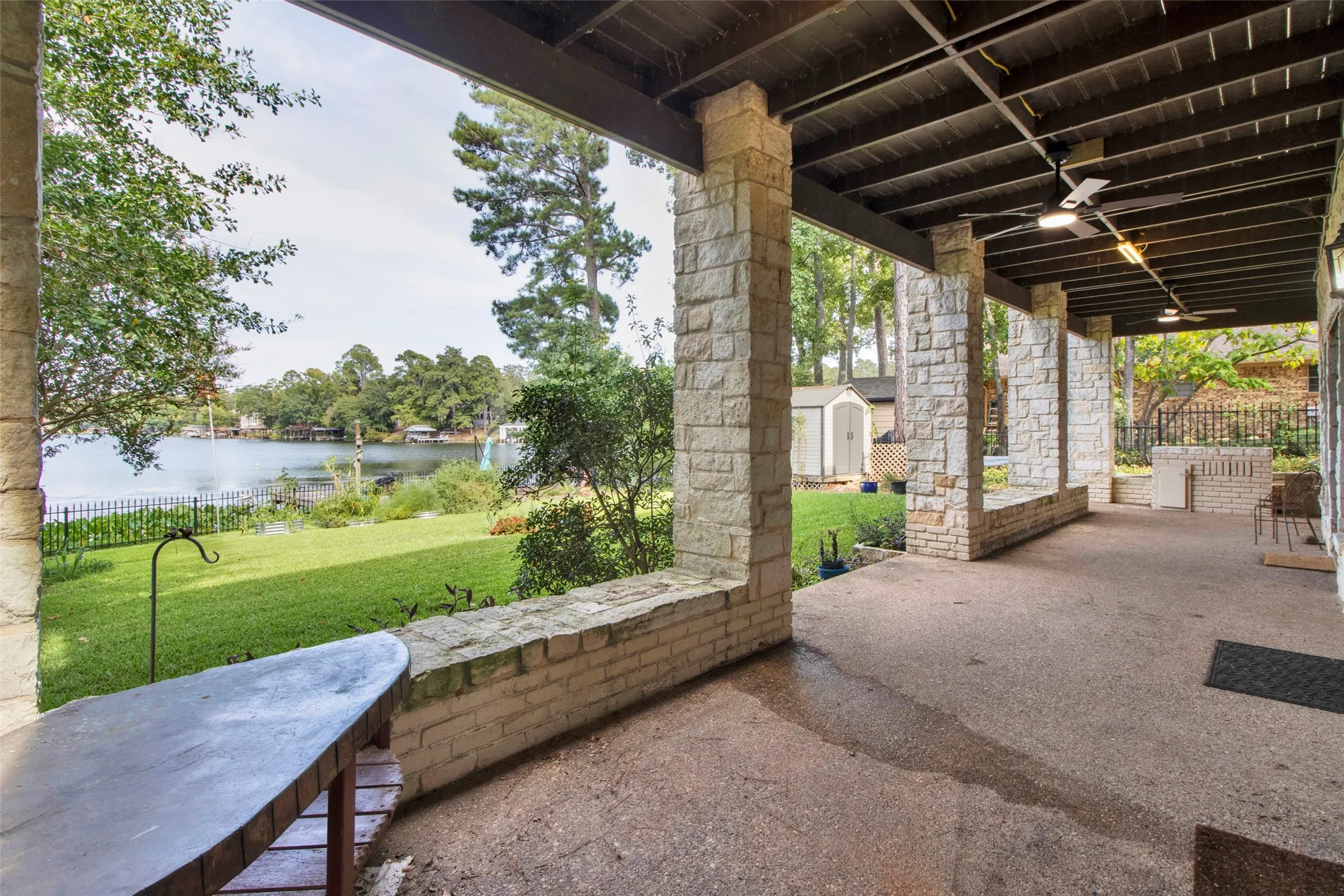 Expansive covered patio with stone columns, concrete flooring, and ceiling fans