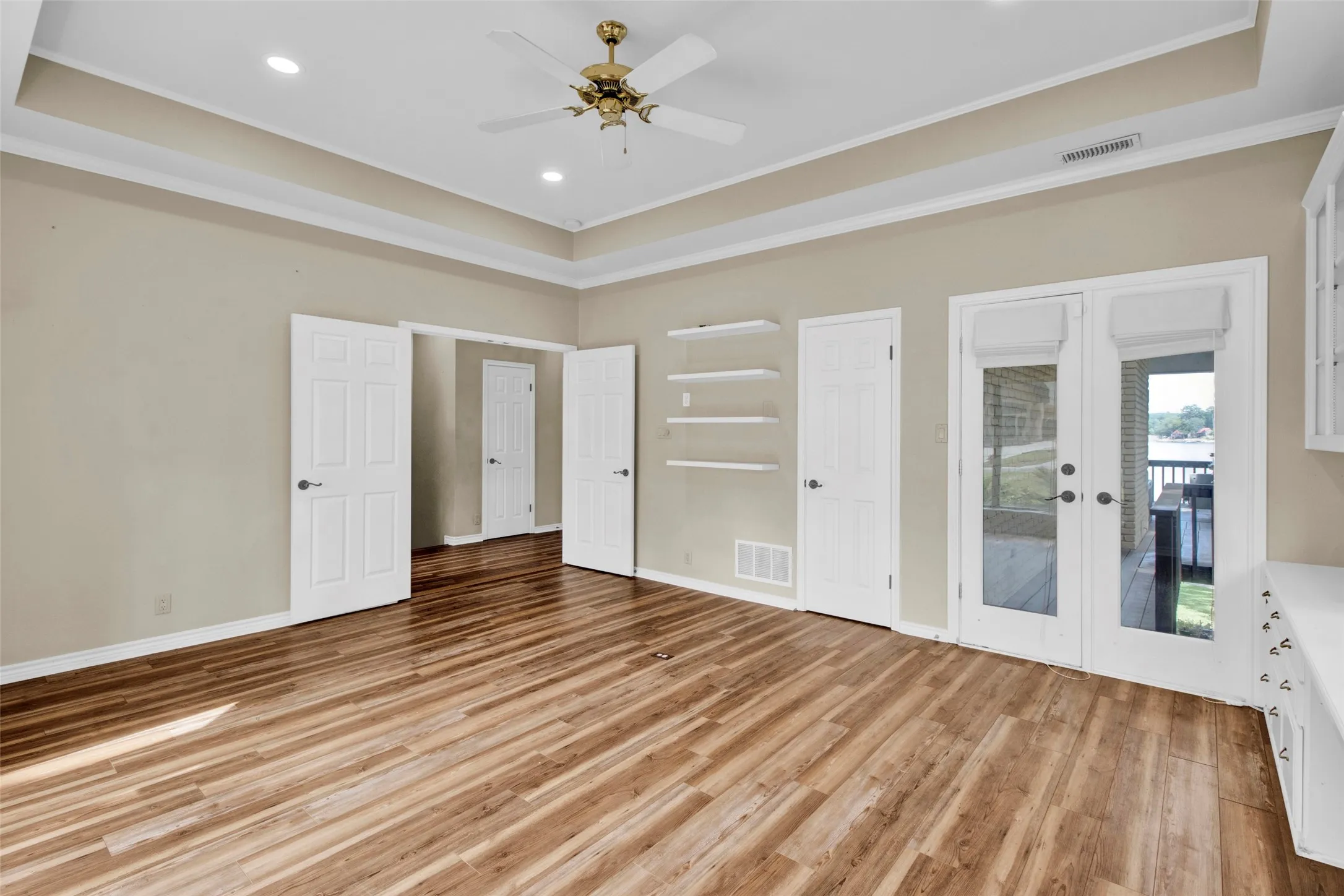Tray ceiling with recessed lighting and a ceiling fan, wood-finish flooring, built-in shelving, built-in cabinetry with a countertop, and glass-paneled French doors