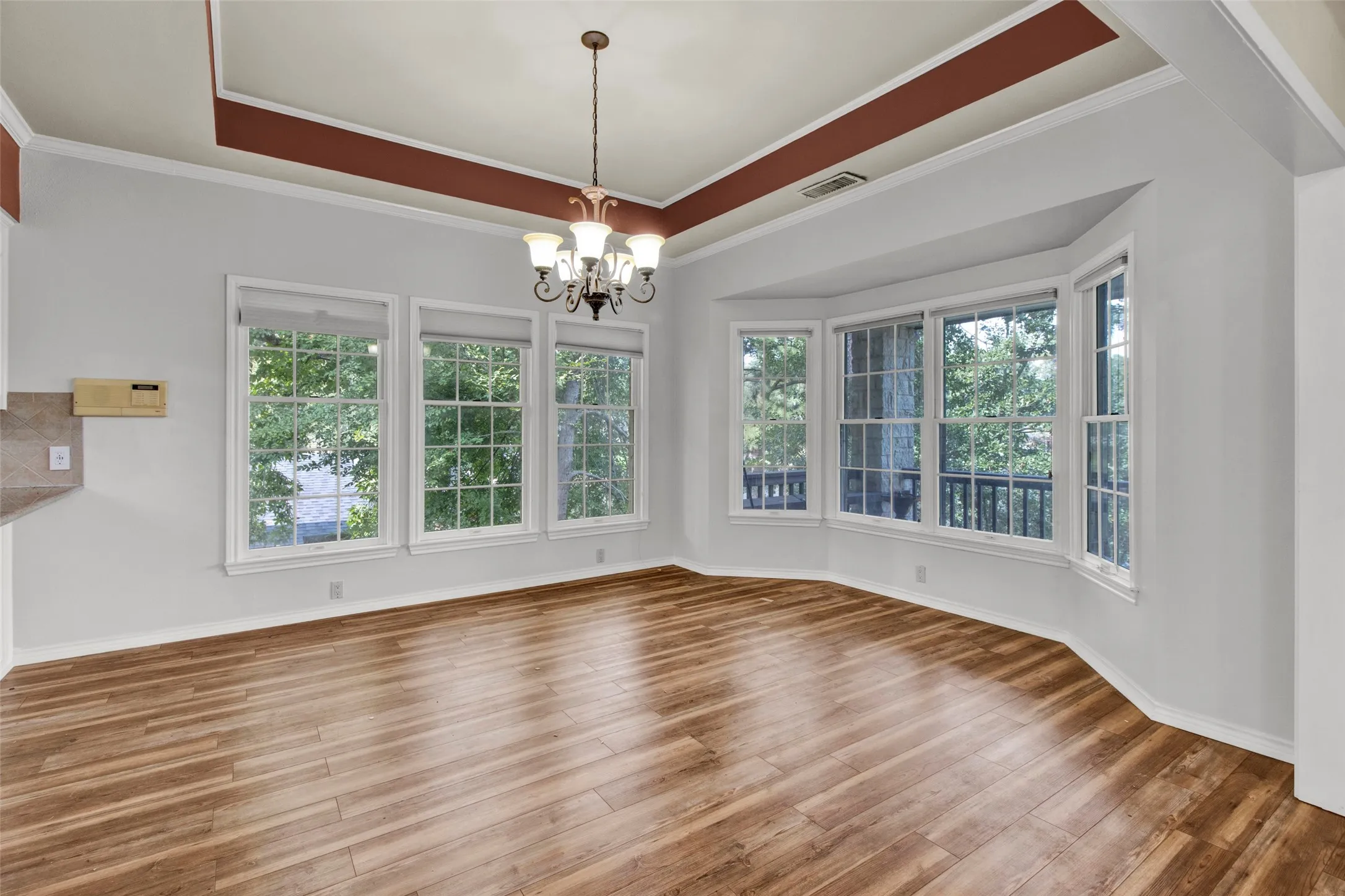Recessed ceiling detail with a decorative chandelier, multiple windows with grid patterns, a bay window feature, and wood-finish flooring