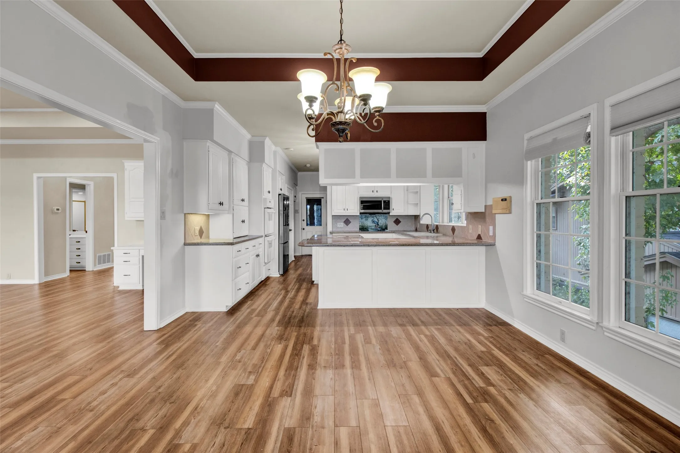 Spacious room featuring wood-finish flooring, a coffered ceiling, and a kitchen area with white cabinetry, stainless steel appliances, and a tiled backsplash