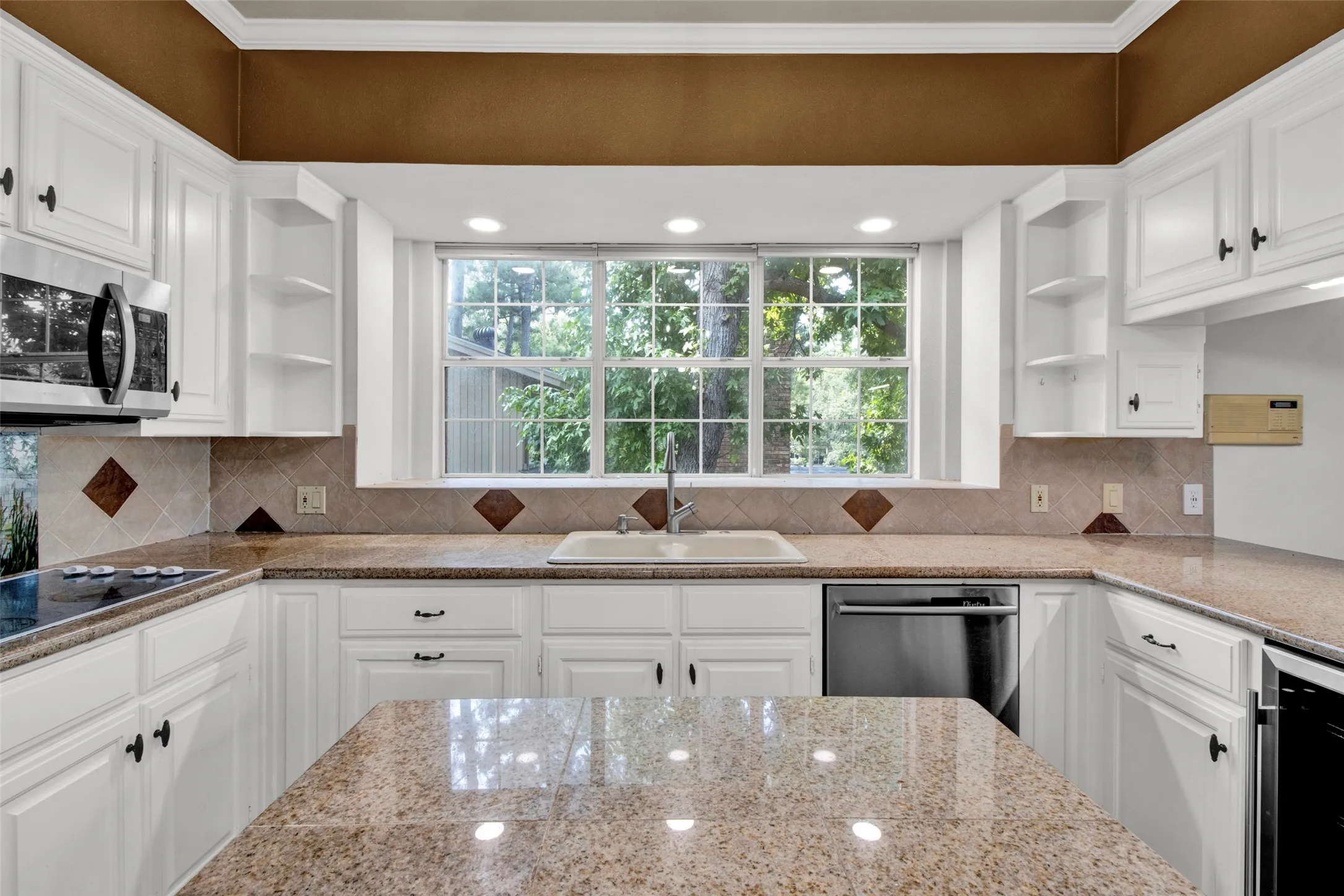 White cabinetry with black hardware, granite countertops, and a tiled backsplash with diamond accents