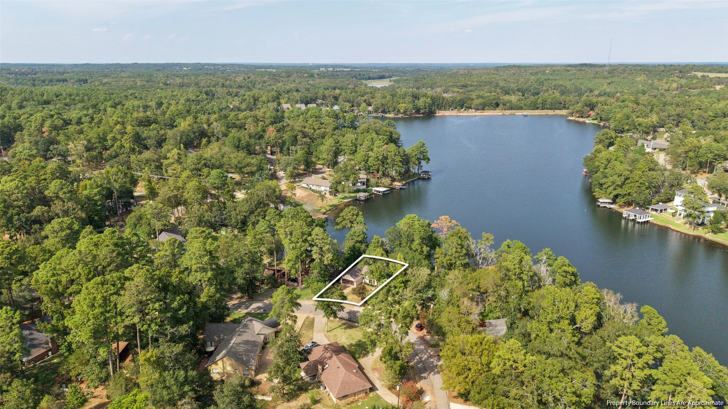 Lakeside property bordered by mature trees, featuring a prominent waterfront and surrounding wooded landscape