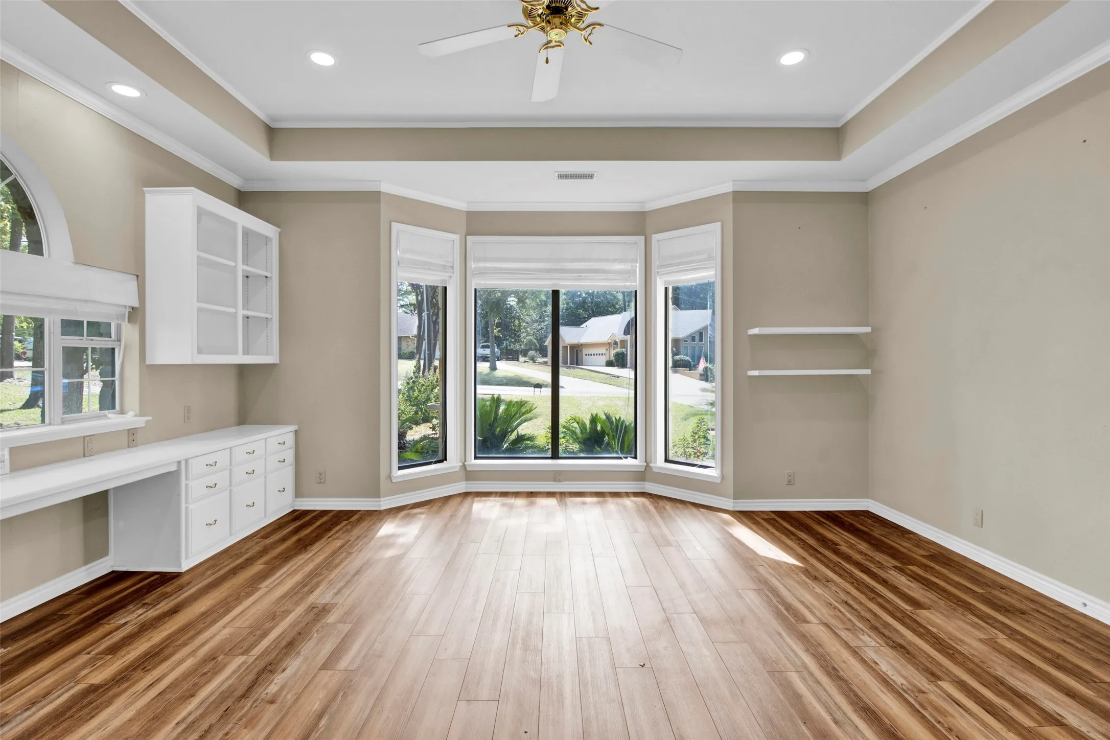 Wood-finish flooring, built-in cabinetry, recessed lighting, ceiling fan, and a large bay window