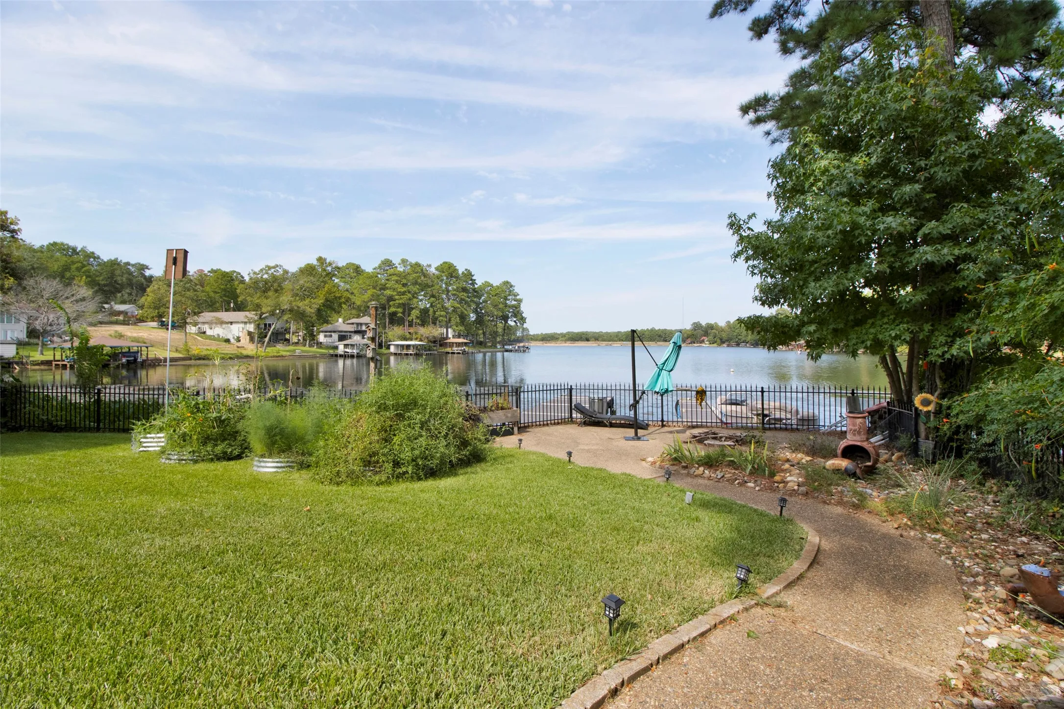 Lakeside property featuring a manicured lawn, a winding stone-edged pathway, a black wrought-iron fence, and direct lake access