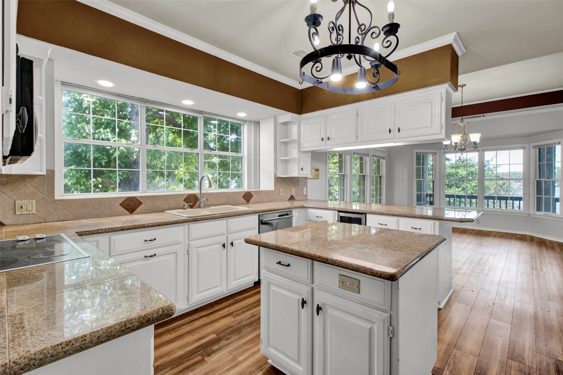 White cabinetry, granite countertops, tile backsplash, wood-finish flooring, and an island with additional storage