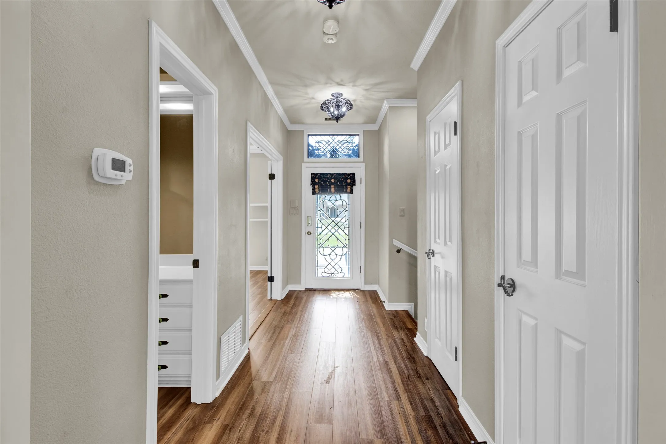 Wood-finish flooring extending throughout, crown molding, and a decorative front door with transom window