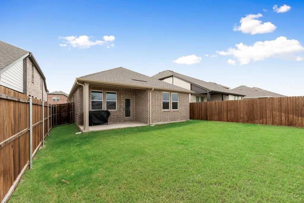 Expansive green lawn with a covered concrete patio, brick exterior, and wood privacy fencing