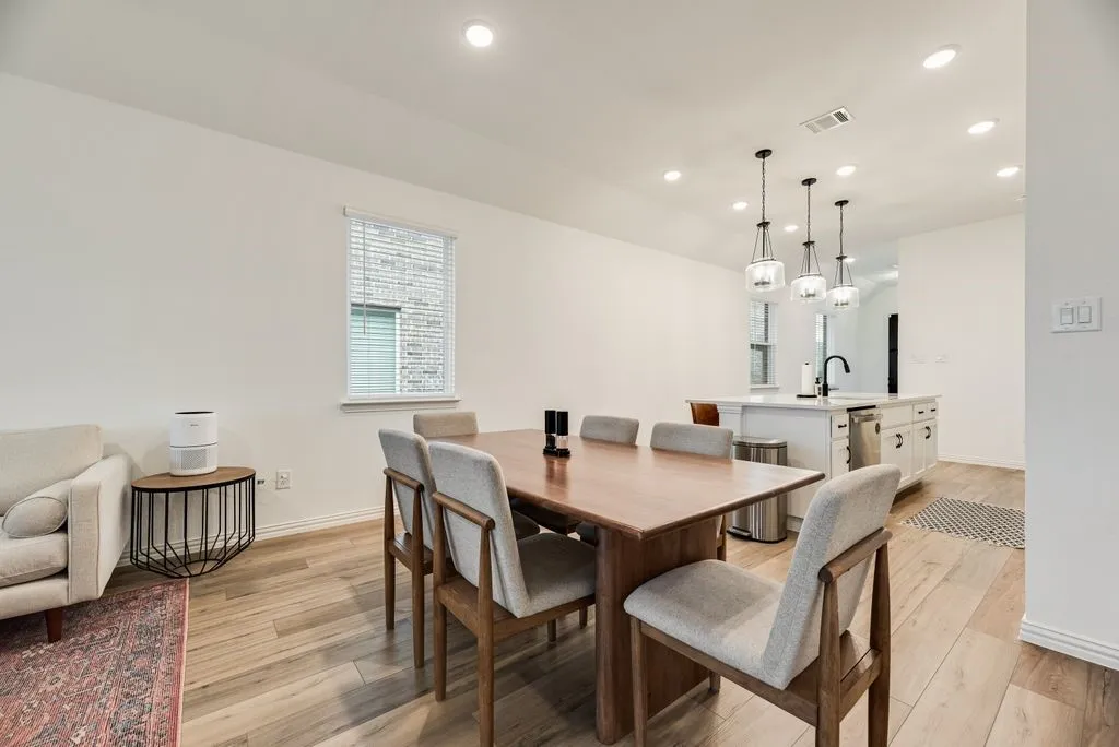 Open-concept living space with wood-finish flooring, recessed lighting, and a kitchen island featuring pendant lighting and a built-in sink