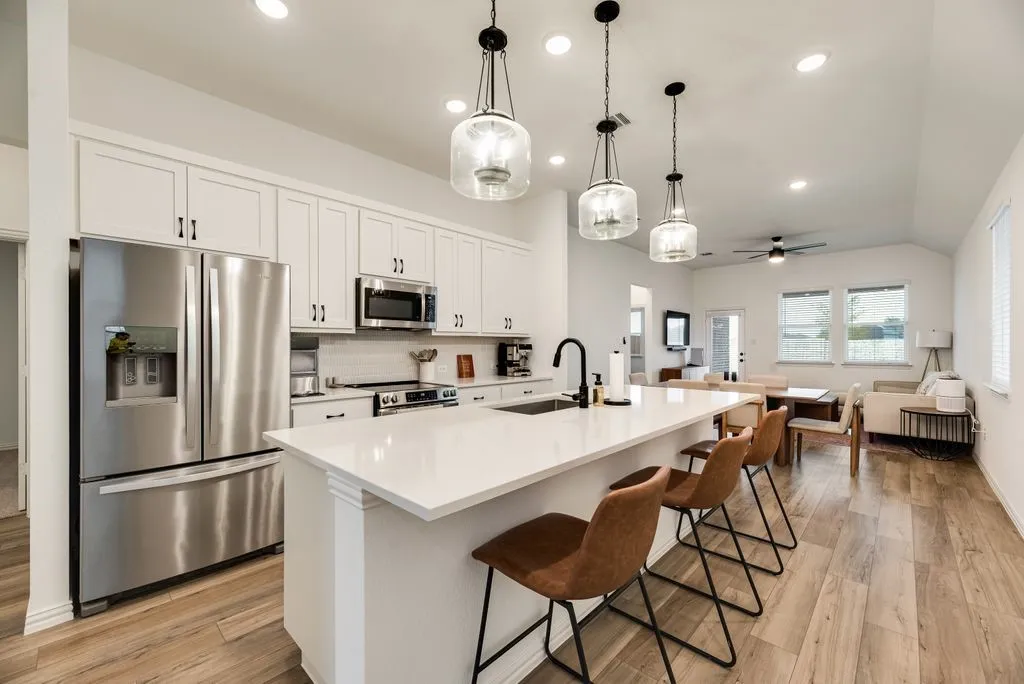 Spacious kitchen featuring an expansive island, stainless steel appliances, white cabinetry with dark hardware, and wood-finish flooring