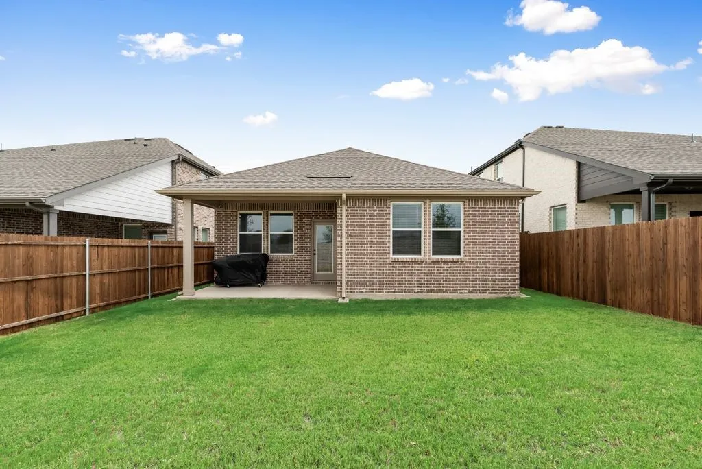 Expansive grassy yard with wood fencing, brick exterior, covered patio, and multiple windows