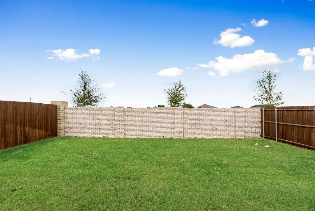Expansive grassy yard with a light-colored brick privacy wall and wood fence