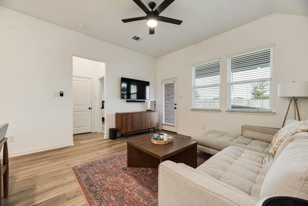 Wood-finish flooring, vaulted ceiling, black ceiling fan, white window blinds, and a glass-paneled door