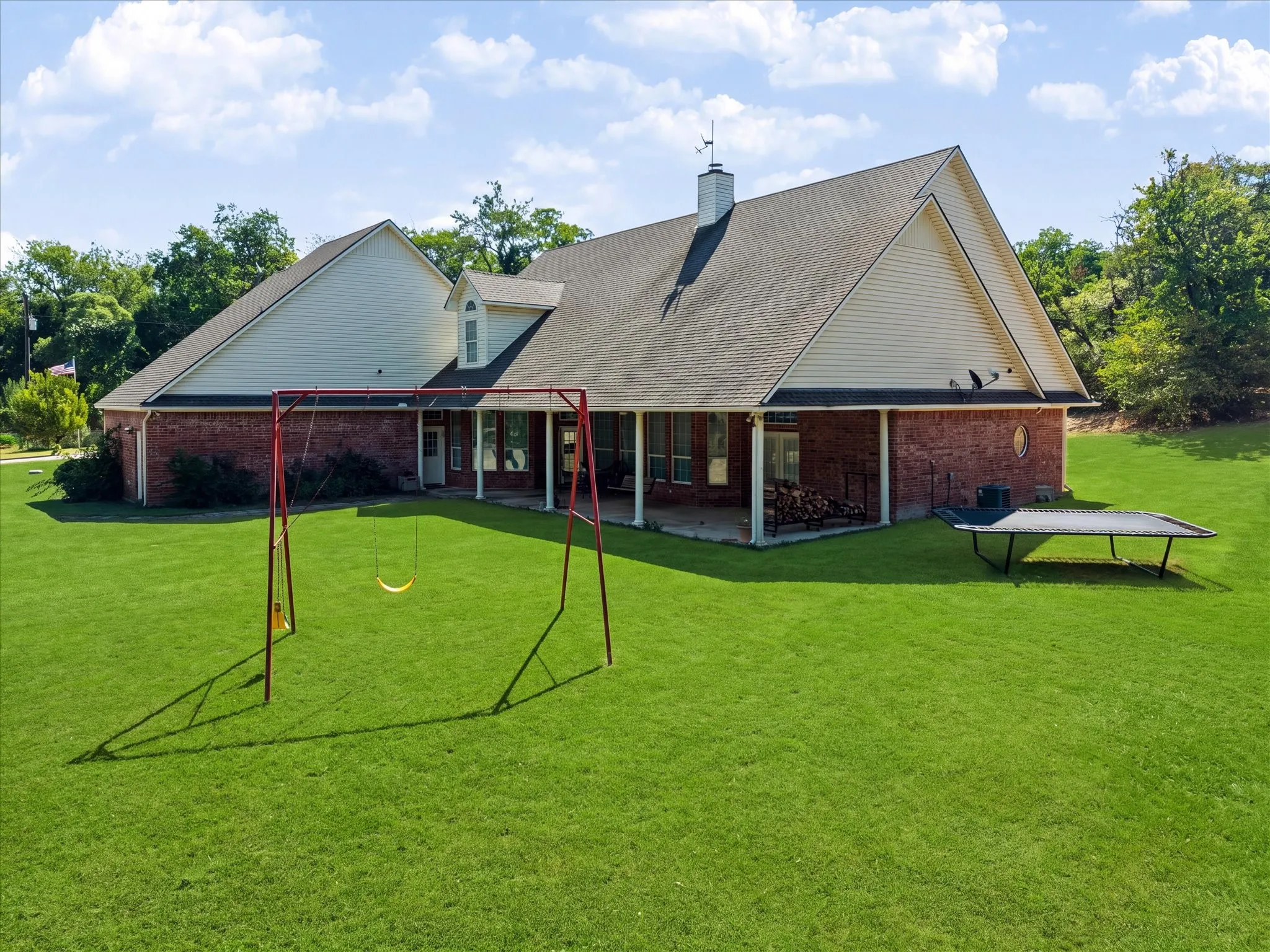 Expansive lawn surrounding a brick exterior home with a covered patio, dormer window, and chimney