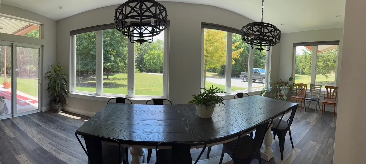Expansive windows with roller shades, wood-finish flooring, two decorative chandeliers, and recessed lighting