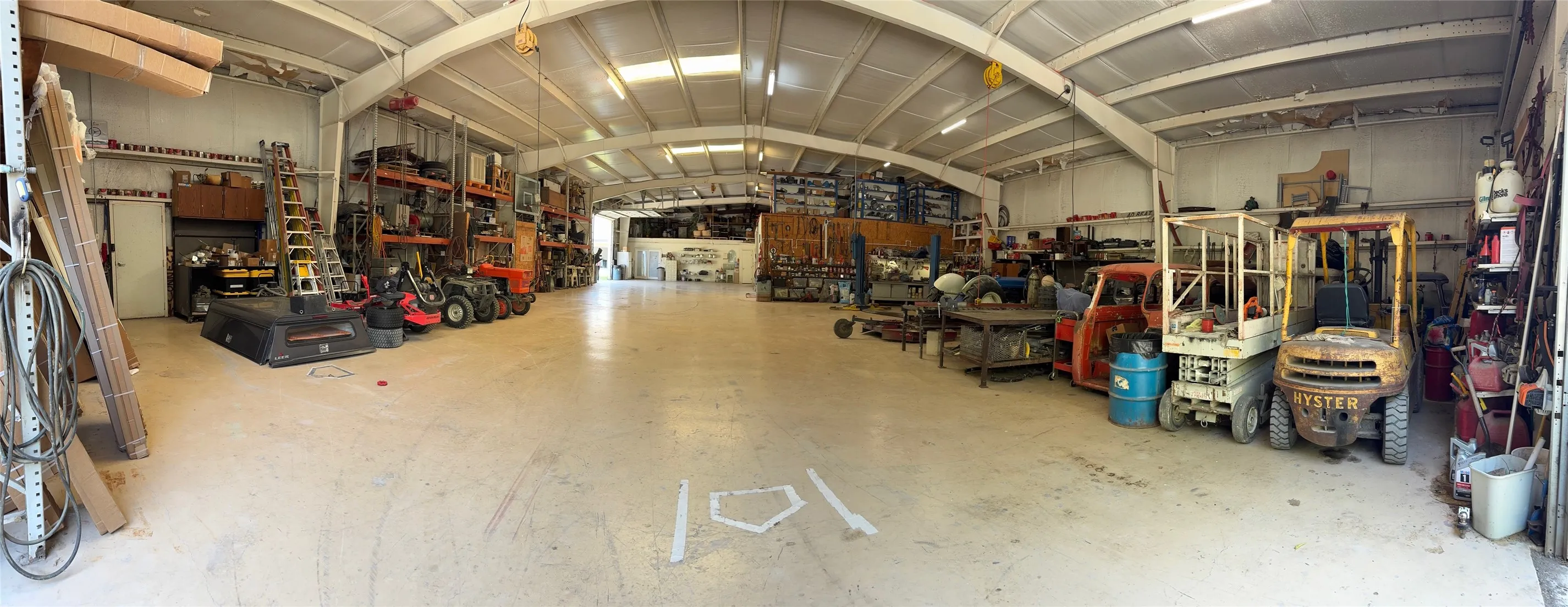 Spacious industrial interior featuring a high arched ceiling, exposed metal framing, concrete flooring, and overhead lighting fixtures