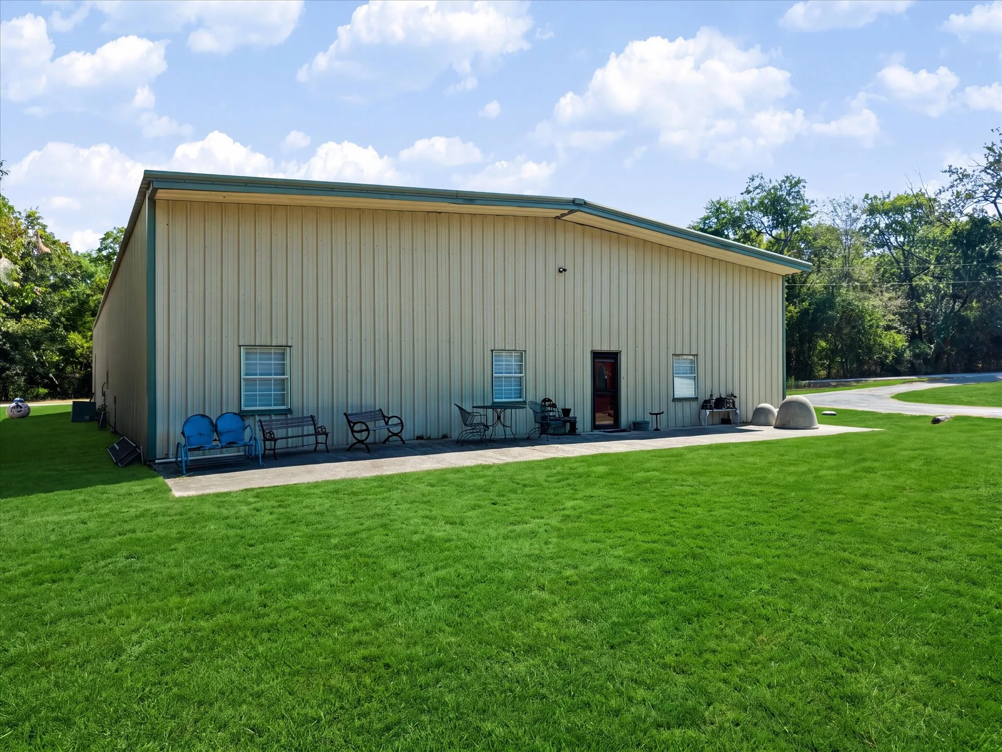 Metal exterior building with a pitched roof, multiple windows, a solid entry door, a concrete patio, and a manicured lawn