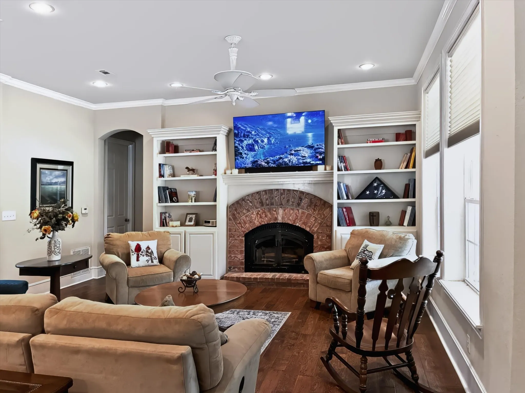 Hardwood flooring throughout, featuring a brick fireplace with an arched opening, built-in shelving, and recessed lighting