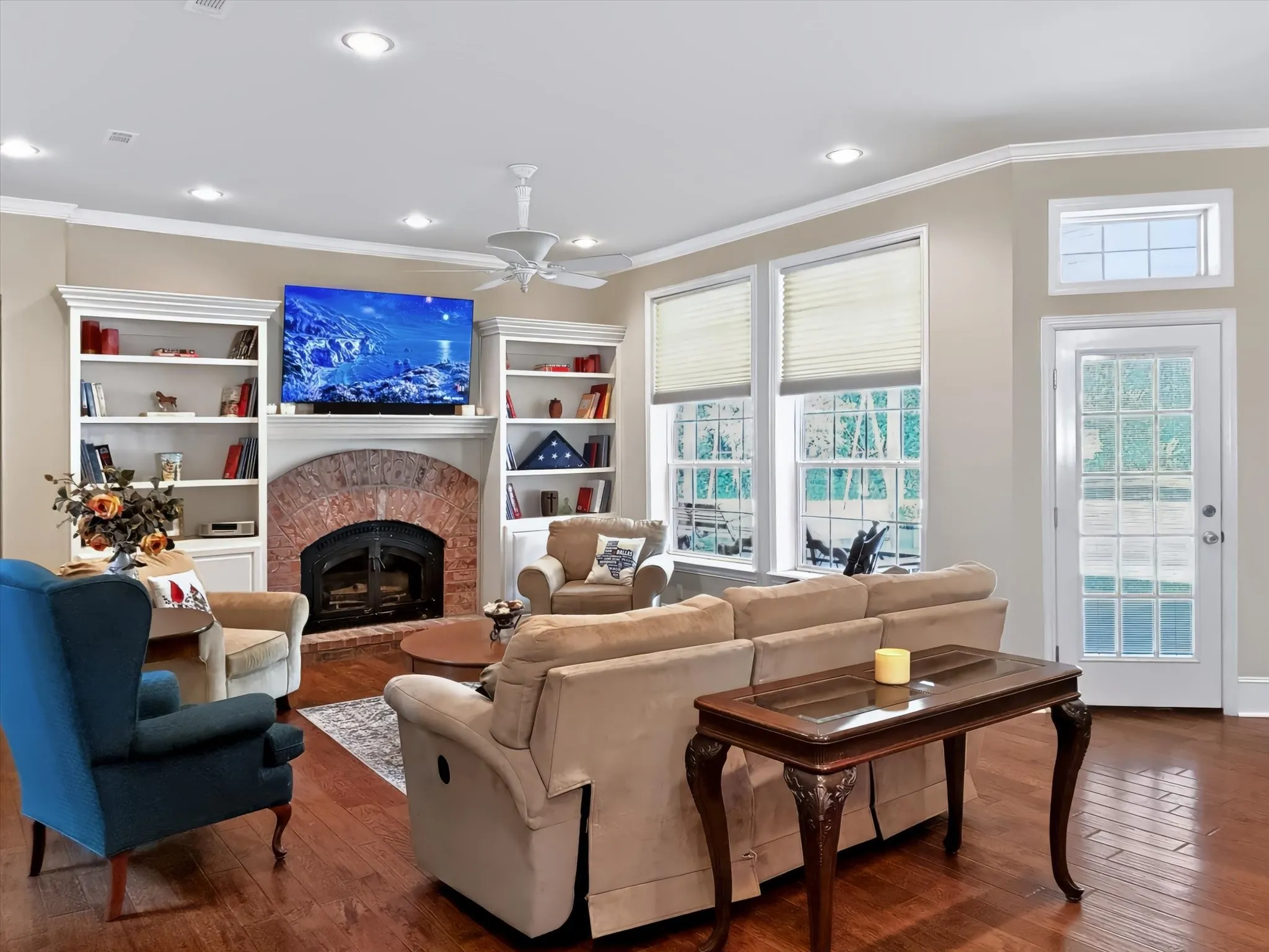 Living area featuring wood-finish flooring, a brick-surround fireplace, built-in shelving, recessed lighting, and a glass-paneled exterior door