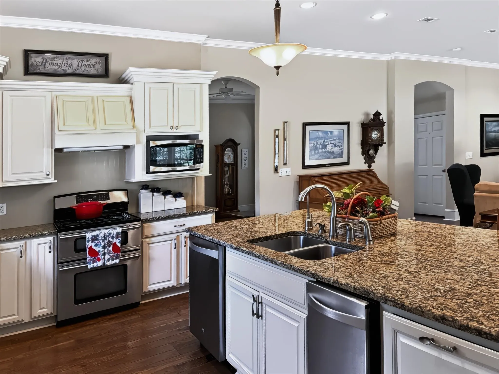 Kitchen with wood-finish flooring, white cabinetry, stainless steel appliances, and a central island featuring a double-basin sink and stone-finish countertop