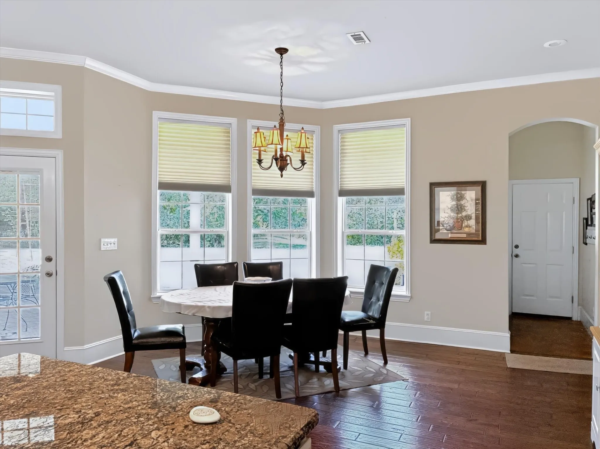 Bay window dining area with wood-finish flooring, an arched entryway, crown molding, and a granite-finish countertop