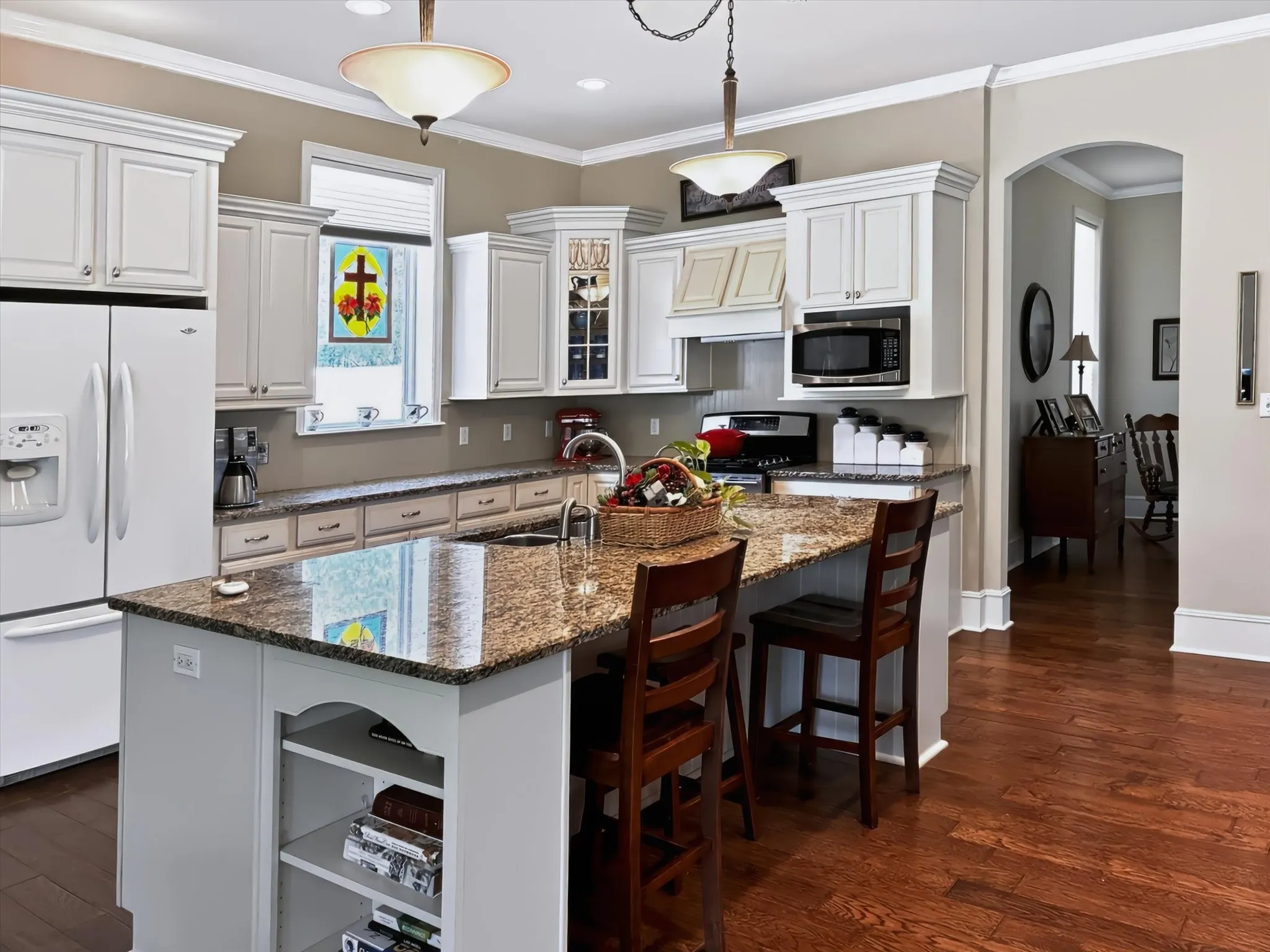 Kitchen featuring a center island with granite countertops, integrated sink, white cabinetry with crown molding, and wood-finish flooring