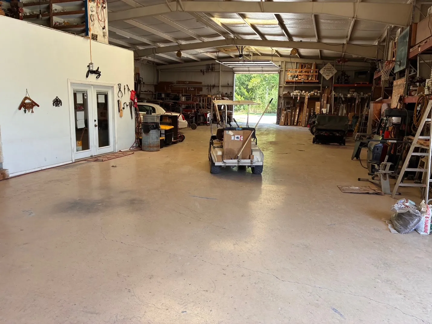 Spacious interior with high ceilings, exposed metal beams, concrete flooring, and a large roll-up door