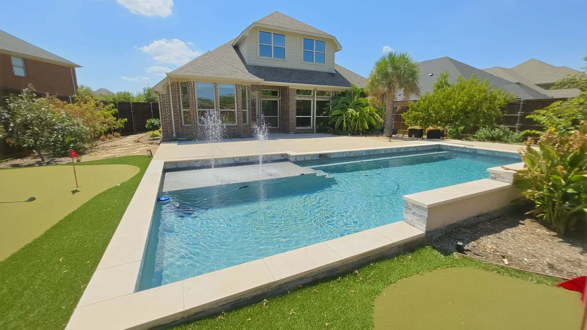Brick and siding exterior with multiple windows, leading to an outdoor pool with water features, a built-in spa, and a putting green