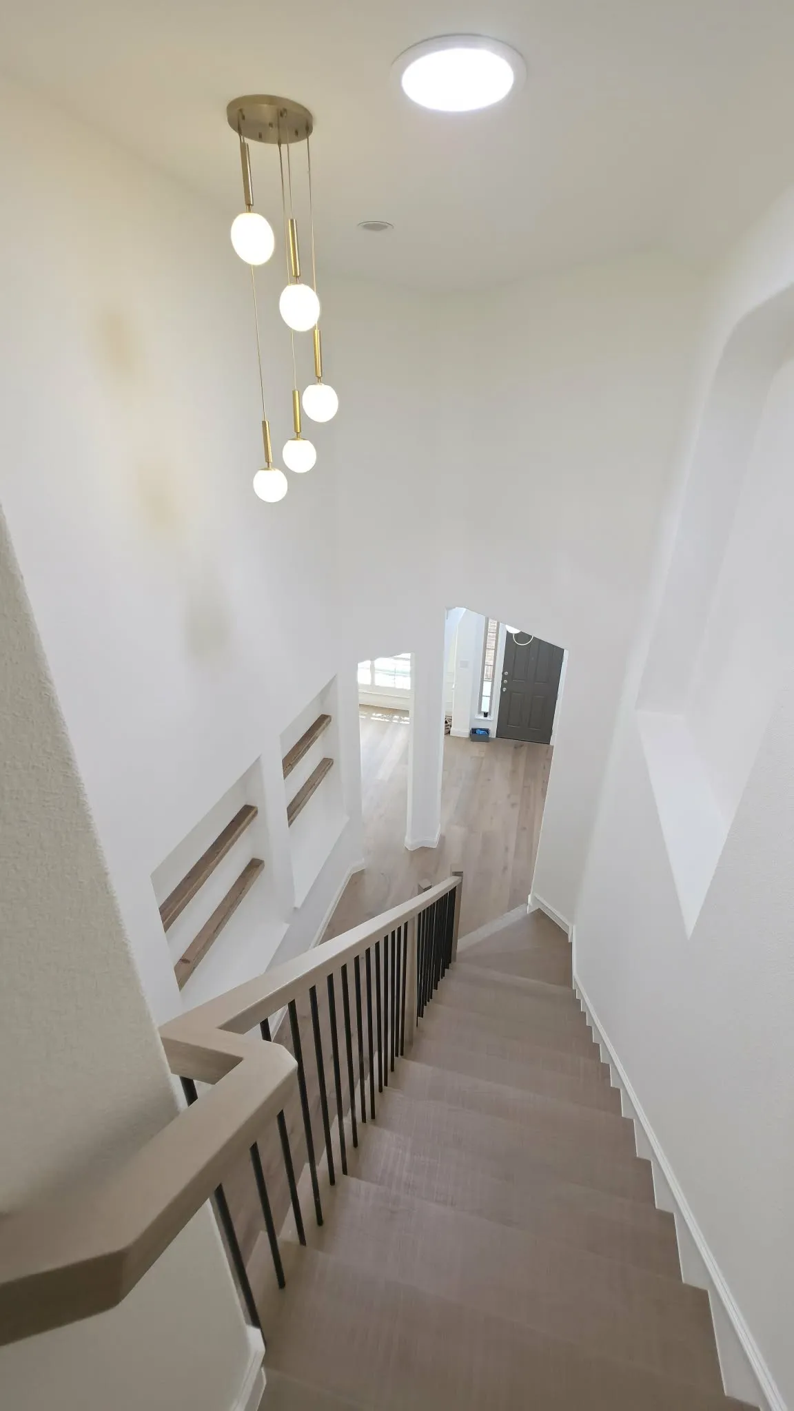 Staircase featuring wood-finish treads and risers, a modern metal and wood-finish railing, and a multi-globe pendant light fixture