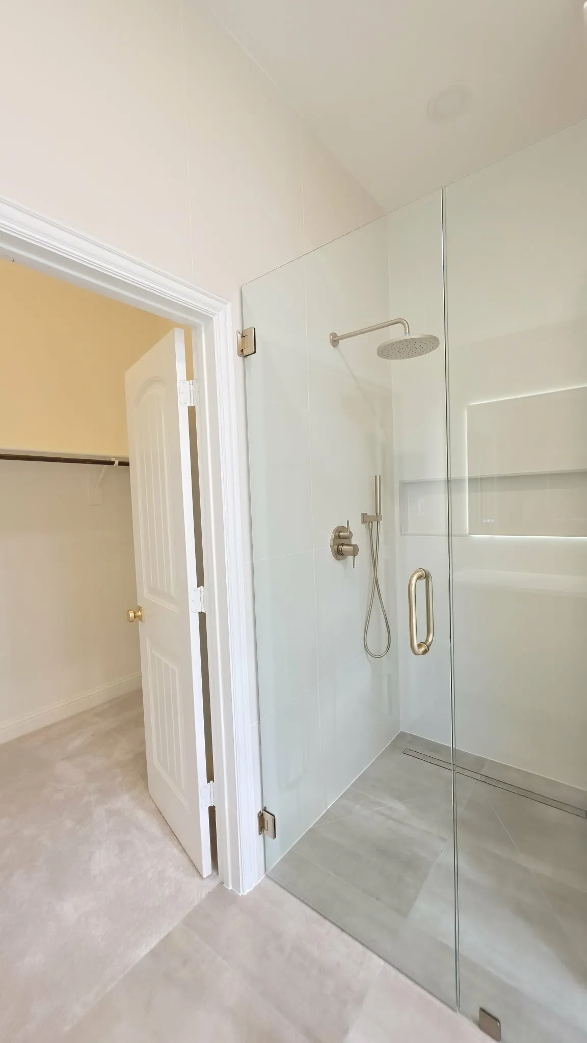 Glass-enclosed shower with a rainfall showerhead, handheld sprayer, recessed shelving, and a linear floor drain