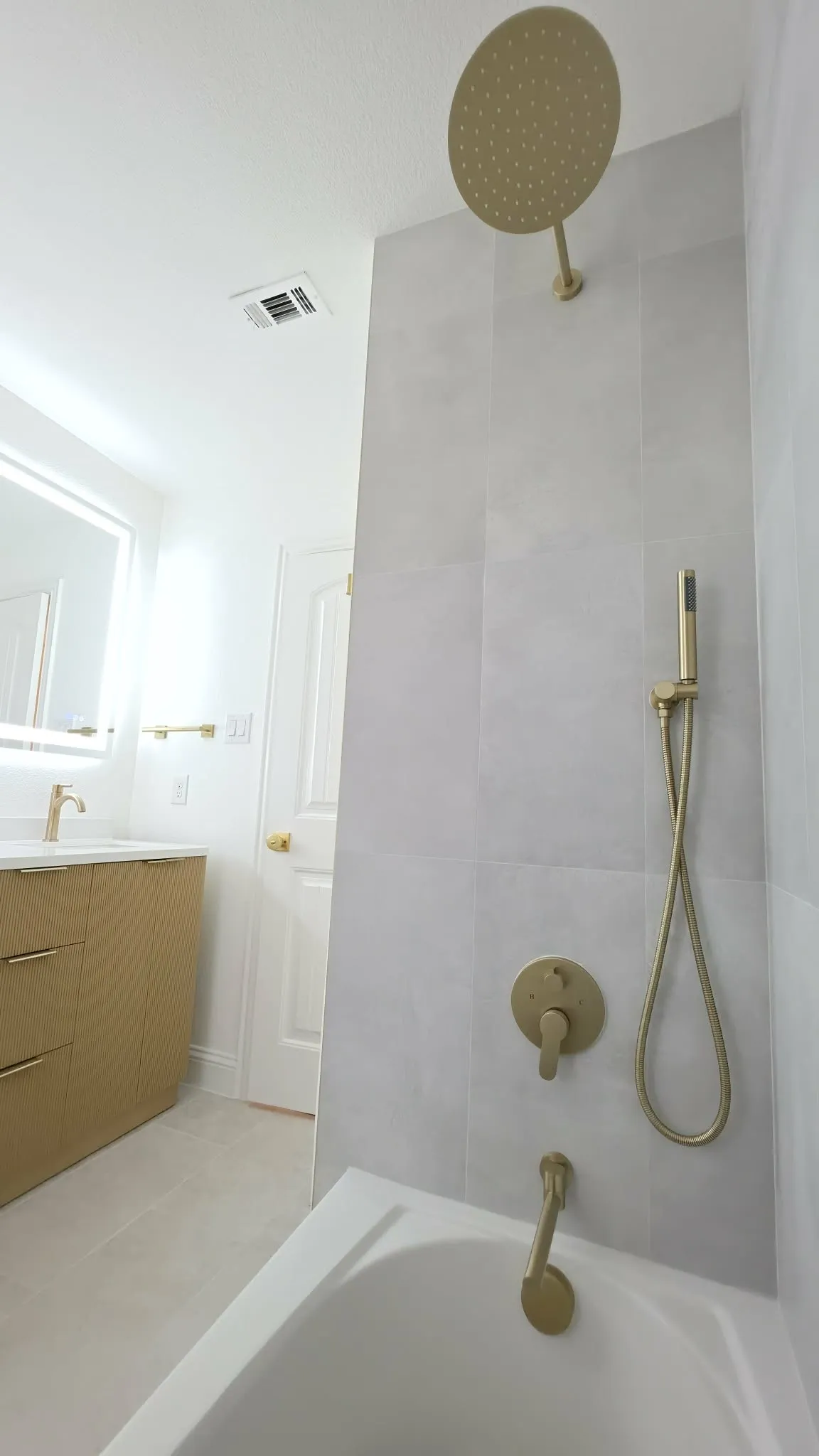 Bathtub with tiled surround, rain shower head, and gold-finish fixtures