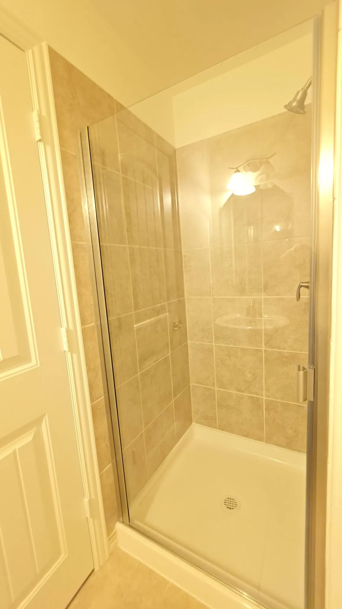 Tiled shower enclosure with a glass door, a shower pan, and a mounted shower head
