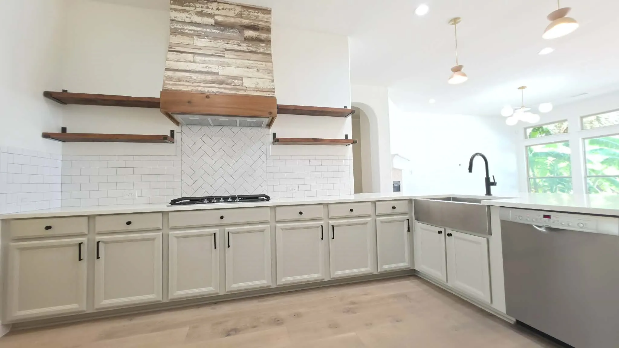 Wood-finish flooring, white cabinetry with black hardware, white subway tile backsplash, stainless steel farmhouse sink, and a stainless steel dishwasher