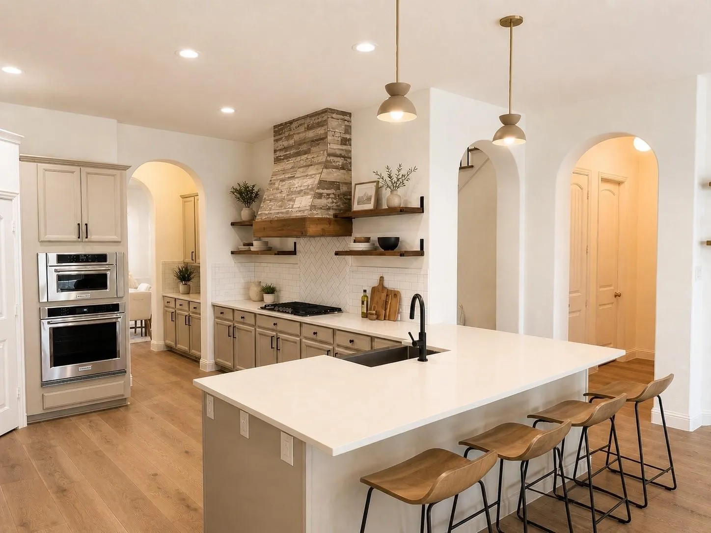 Gourmet kitchen featuring a large central island, stainless steel double ovens, a custom range hood, wood-finish flooring, and arched doorways