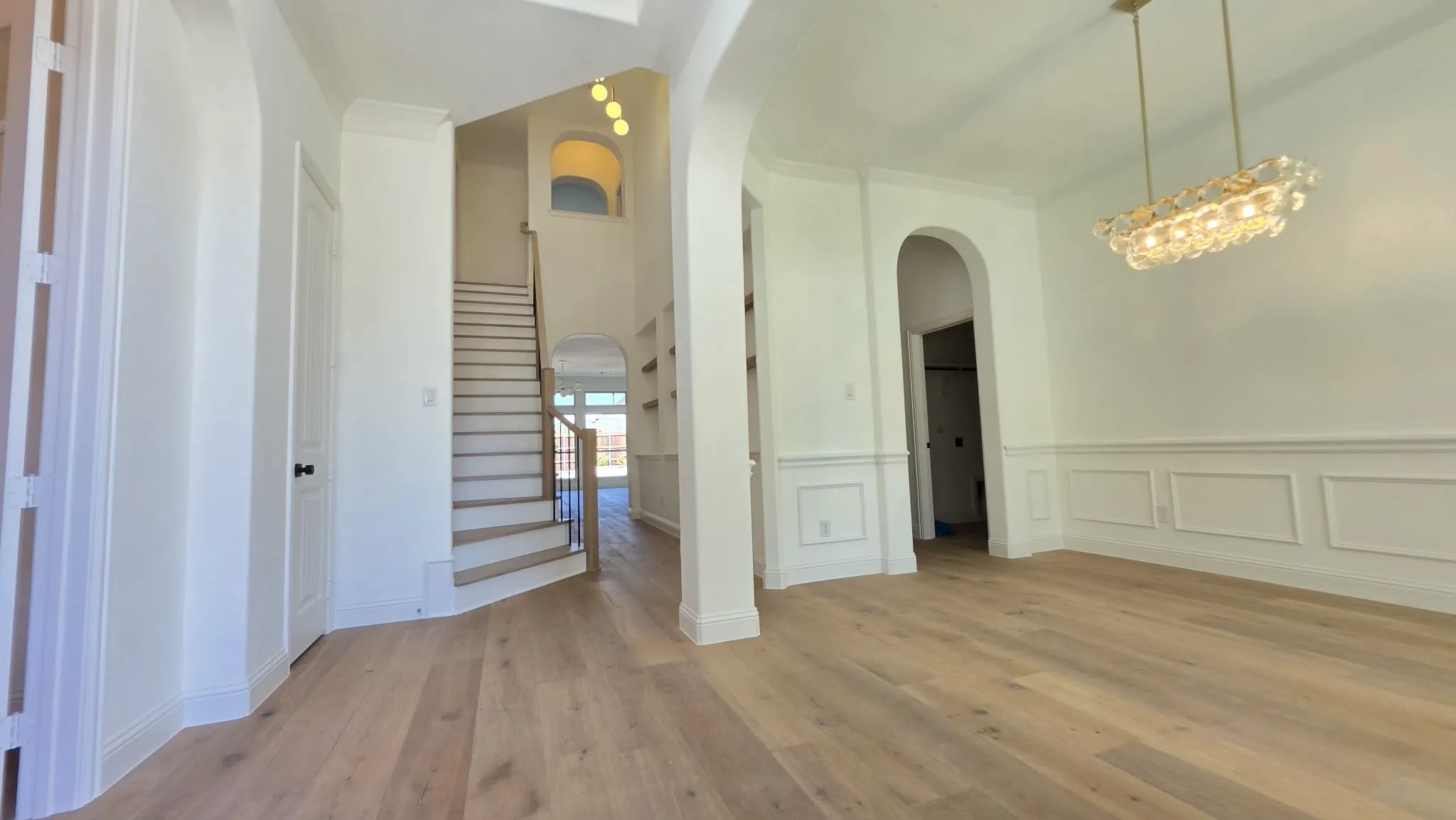 Light wood-finish flooring, wainscoting, arched doorways, a built-in staircase, and a decorative chandelier