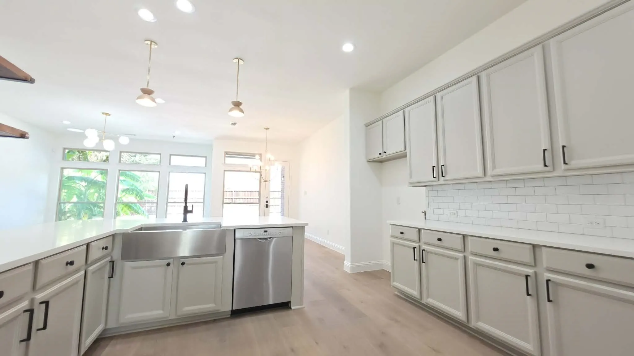 Spacious kitchen featuring an apron front sink, stainless steel dishwasher, wood-finish flooring, white cabinetry, and white subway tile backsplash