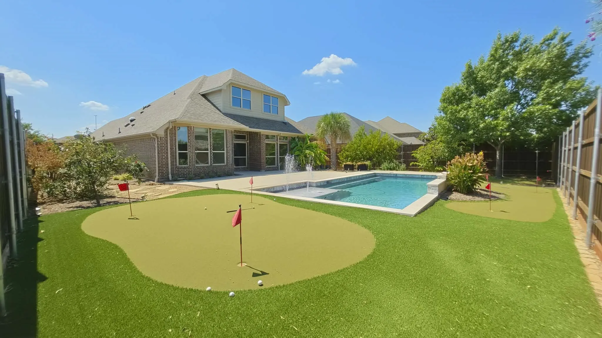 Rear exterior featuring an inground swimming pool with water features, a putting green, and a brick exterior with multiple windows