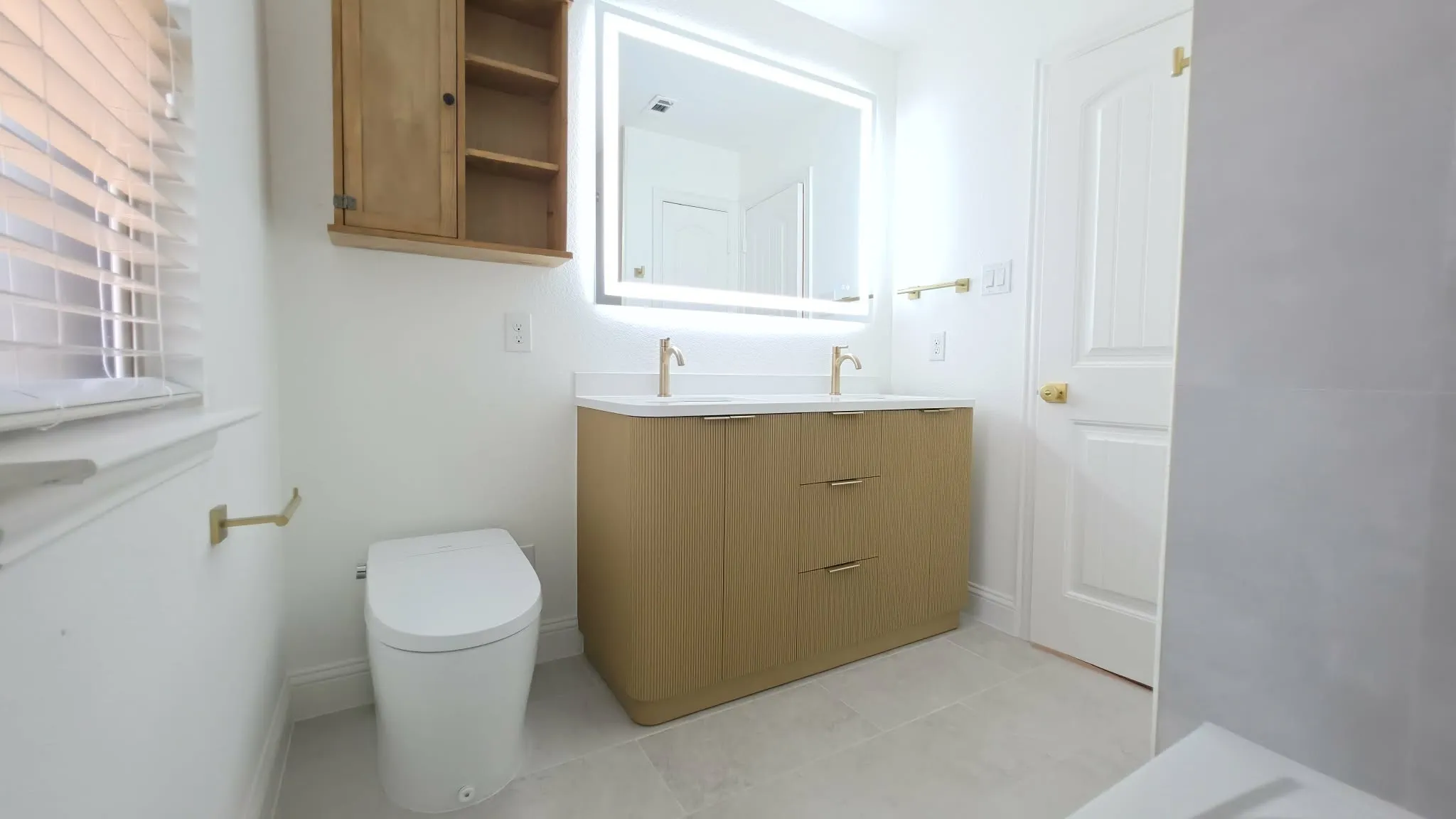 Contemporary vanity with dual basin sinks, illuminated mirror, and gold-finish fixtures