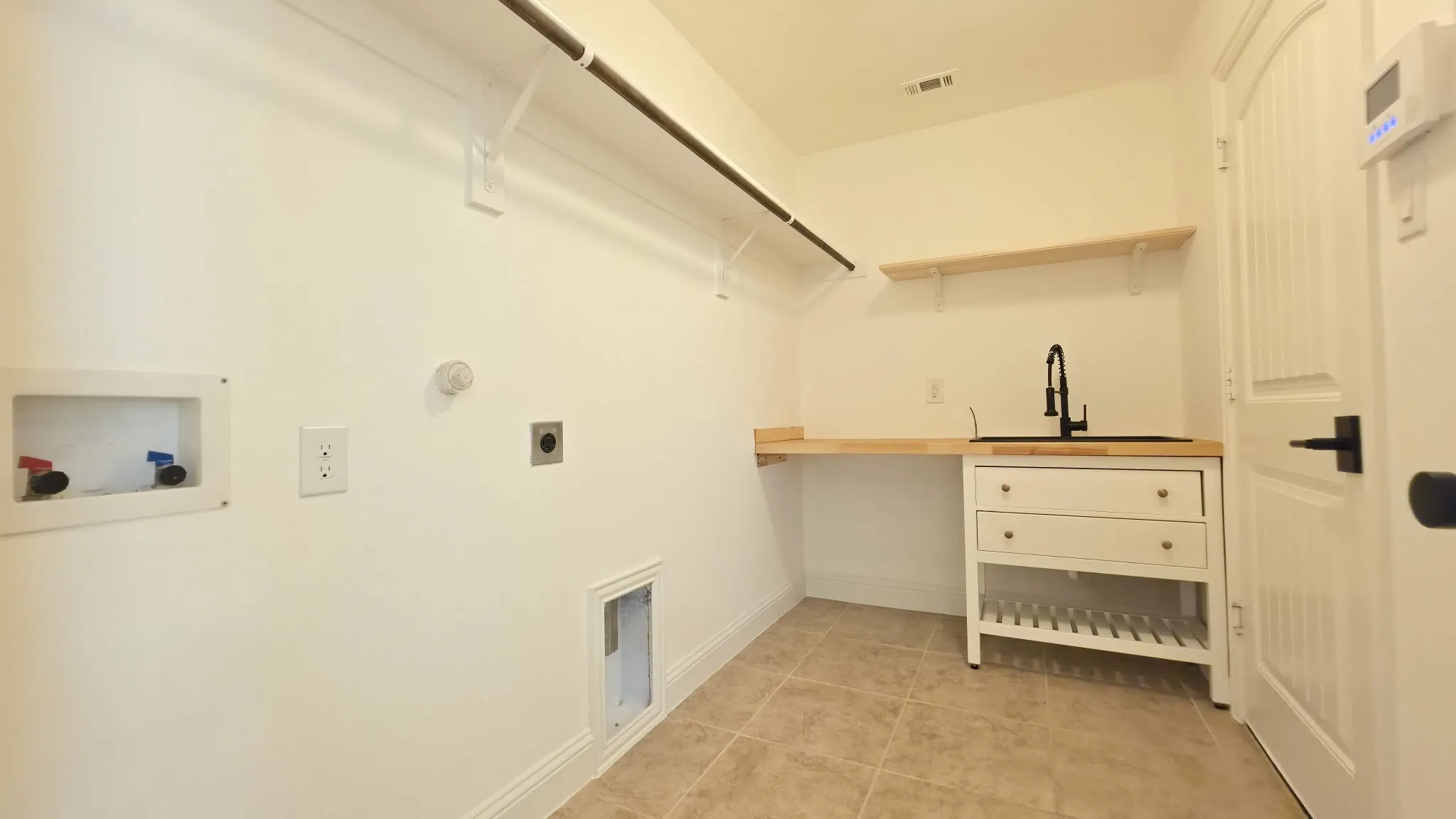 Laundry room featuring tile flooring, a utility sink with a black faucet, a wood-finish countertop, and built-in shelving
